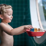 Boy stood in a round window playing with the PlanToys eco-friendly wooden cargo ship toy