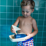 Close up of a young boy holding the PlanToys solid wooden sail boat toy in front of some blue tiles