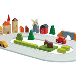 PlanToys plastic-free countryside blocks set and rubber road laid out in a small scene on a white background