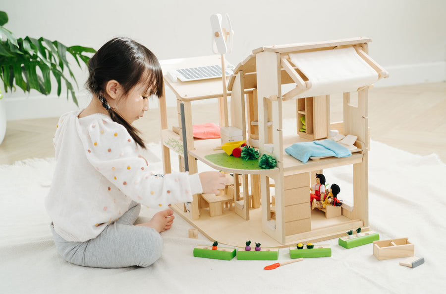 A child sitting besides the PlanToys Green Dolls' House and Furniture Set. The child is reaching for one of the pieces.