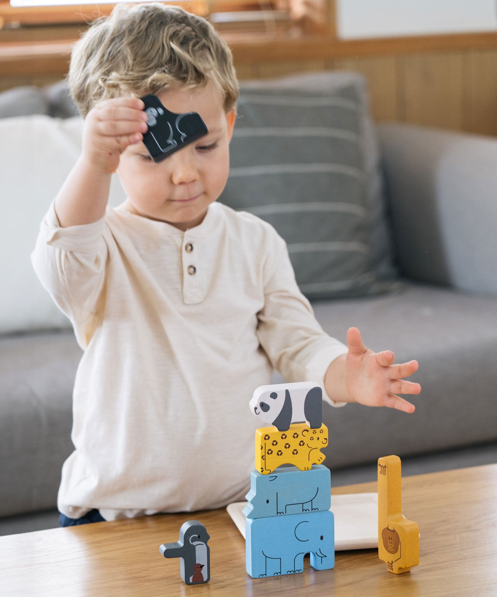 A child stacking the pieces from the Plan Toys Animal Puzzle Game
on a coffee table, he has the black gorilla figure in his hand ready to stack.