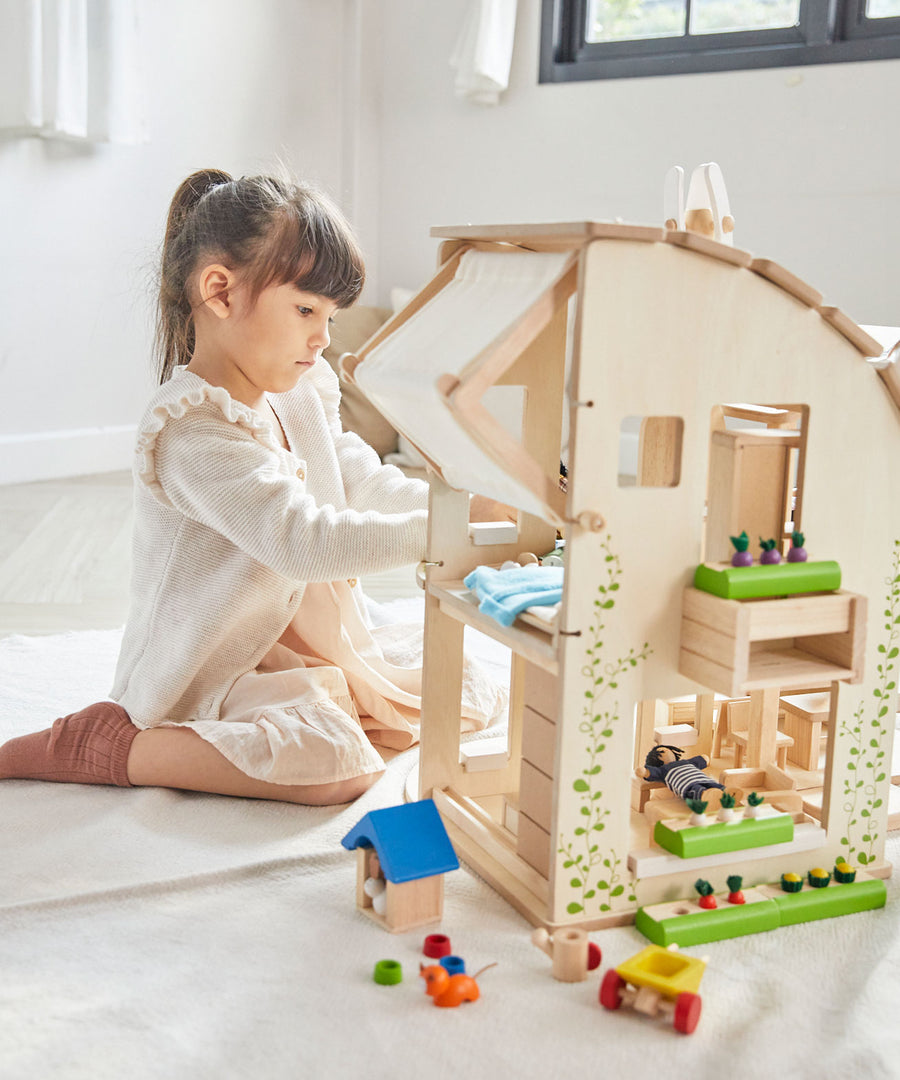 A child sitting besides the PlanToys Green Dolls' House and Furniture Set. 