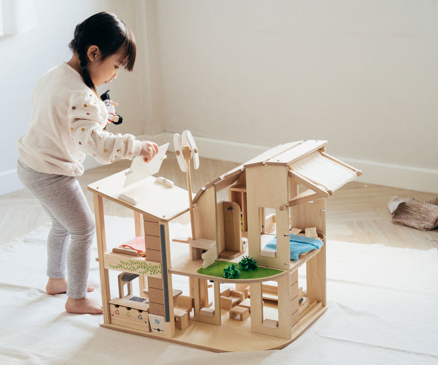 A child standing besides the PlanToys Green Dolls' House and Furniture Set. The child is holding the solar panel in their hand ready to place it back on the roof. 