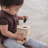 A child sitting on a wooden surface holding the PlanToys Elephant Money Bank upside down. 