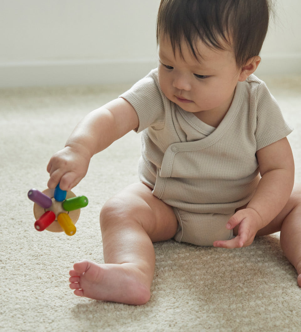 Close up of a toddler sat on the floor holding the PlanToys wooden flexi jellyfish baby toy