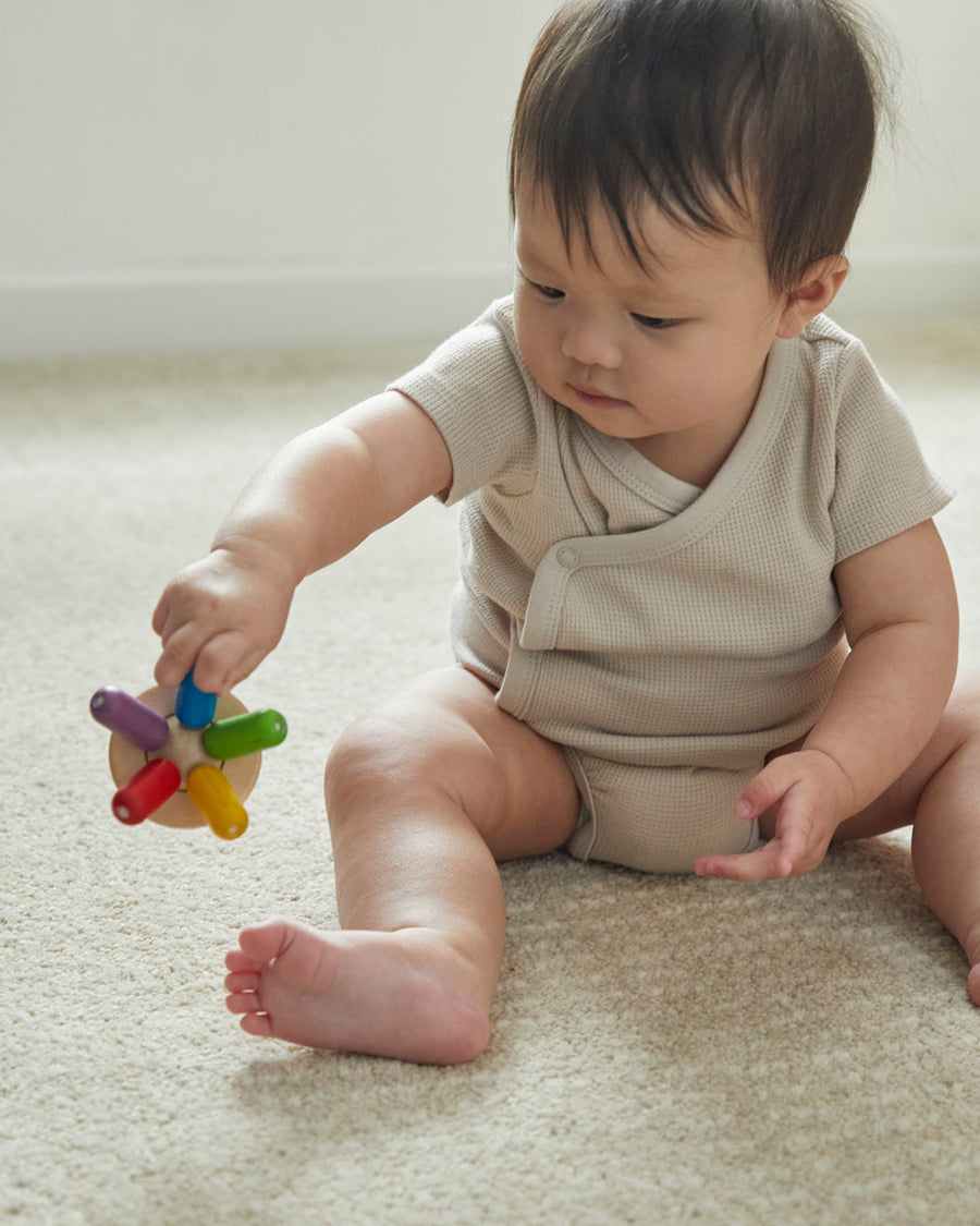 Close up of a toddler sat on the floor holding the PlanToys wooden flexi jellyfish baby toy