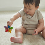 Close up of a toddler sat on the floor holding the PlanToys wooden flexi jellyfish baby toy