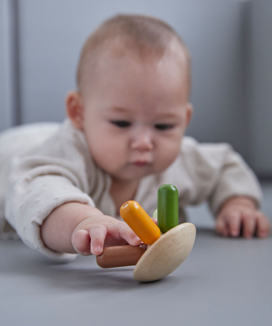 A baby lying on their front playing with the PlanToys flexi jellyfish wooden toy. 