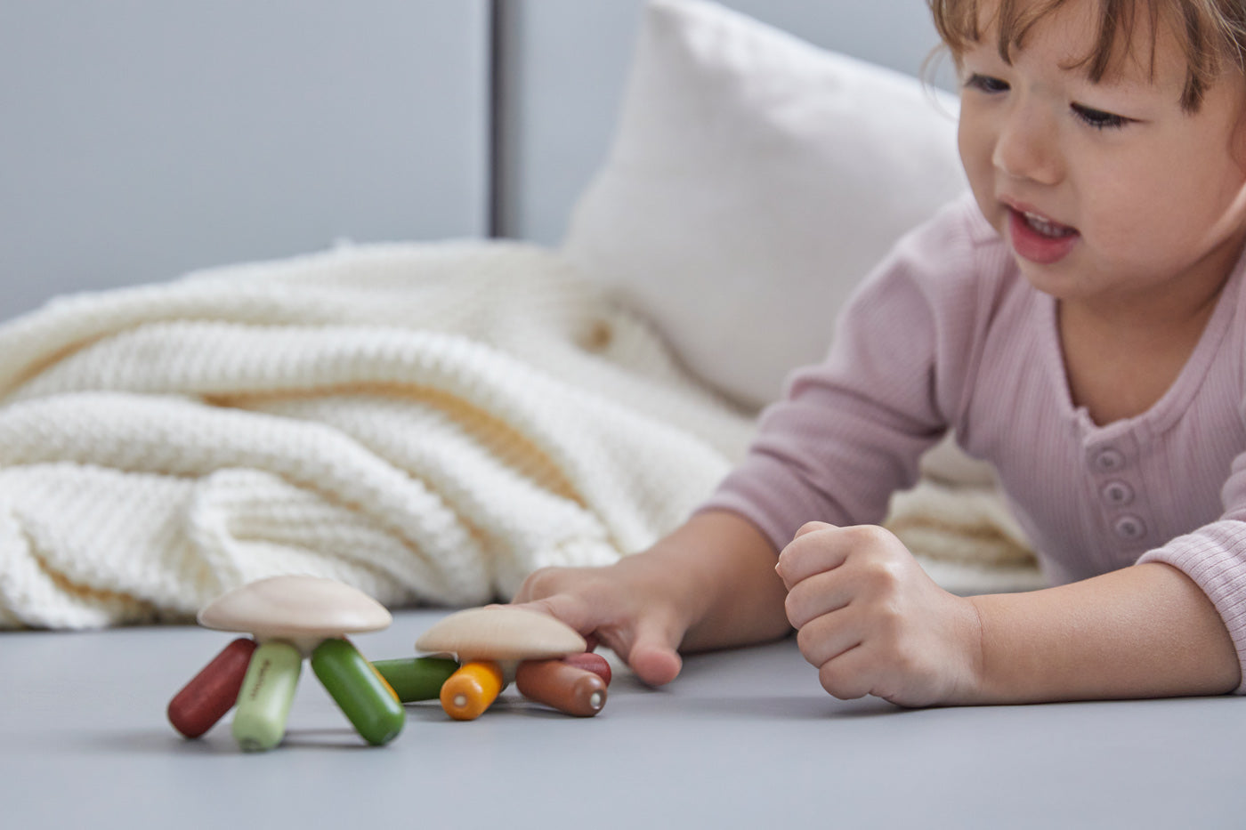 Young girl laying on a grey floor pressing down the top of the PlanToys flexi jellyfish with her finger