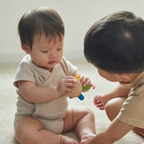 Close up of two young children sat on the floor looking at the PlanToys multicoloured flexi jellyfish baby toy