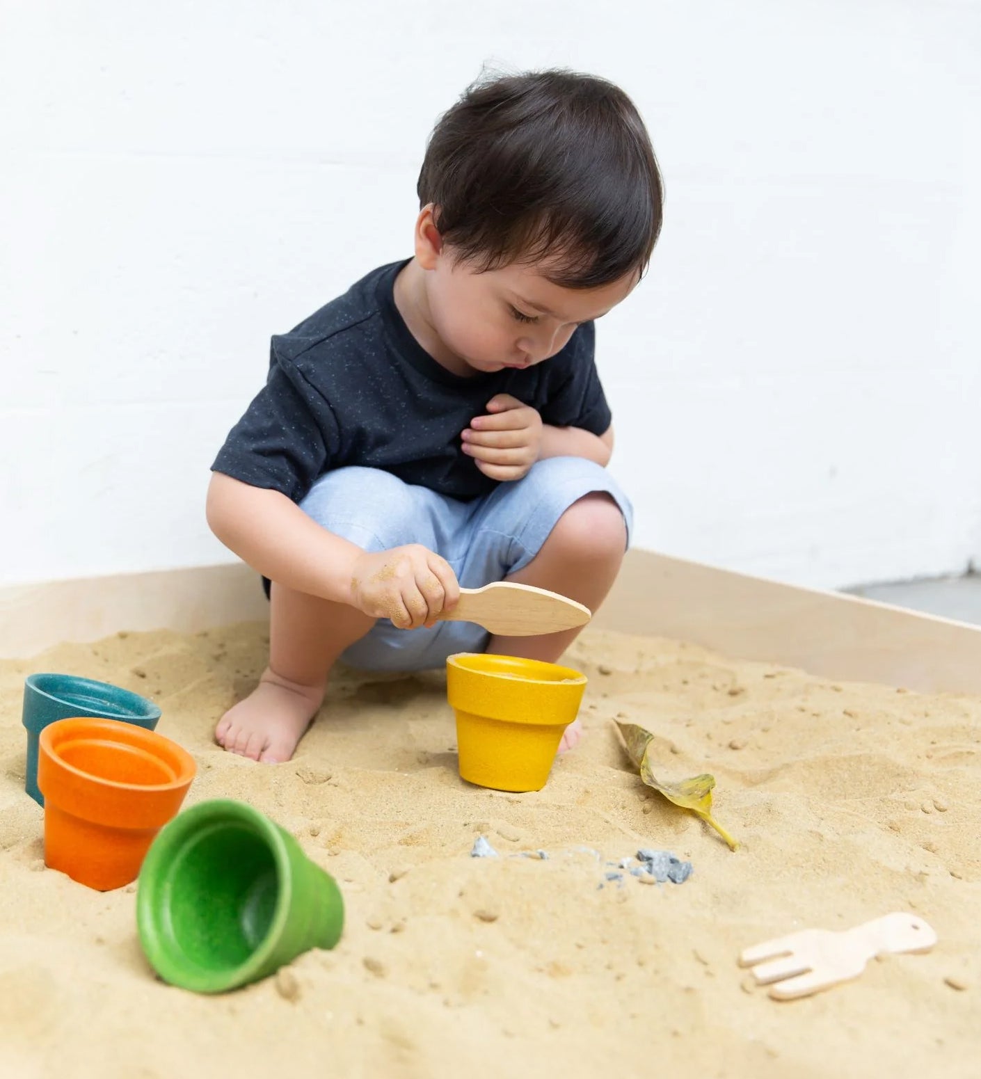 A child playing in a sand pit with the PlanToys flower pots. 