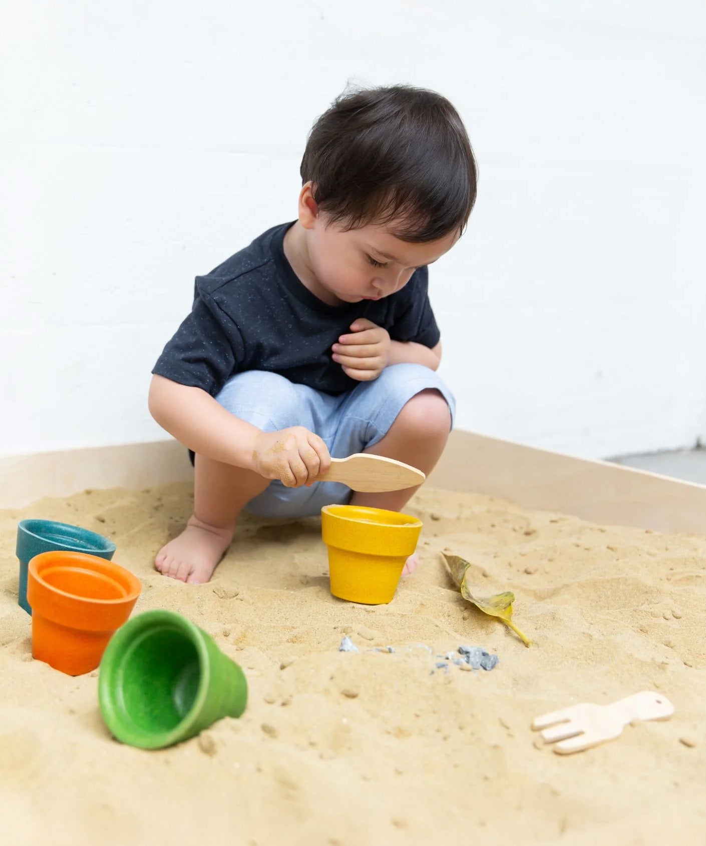 A child playing in a sand pit with the PlanToys flower pots. 