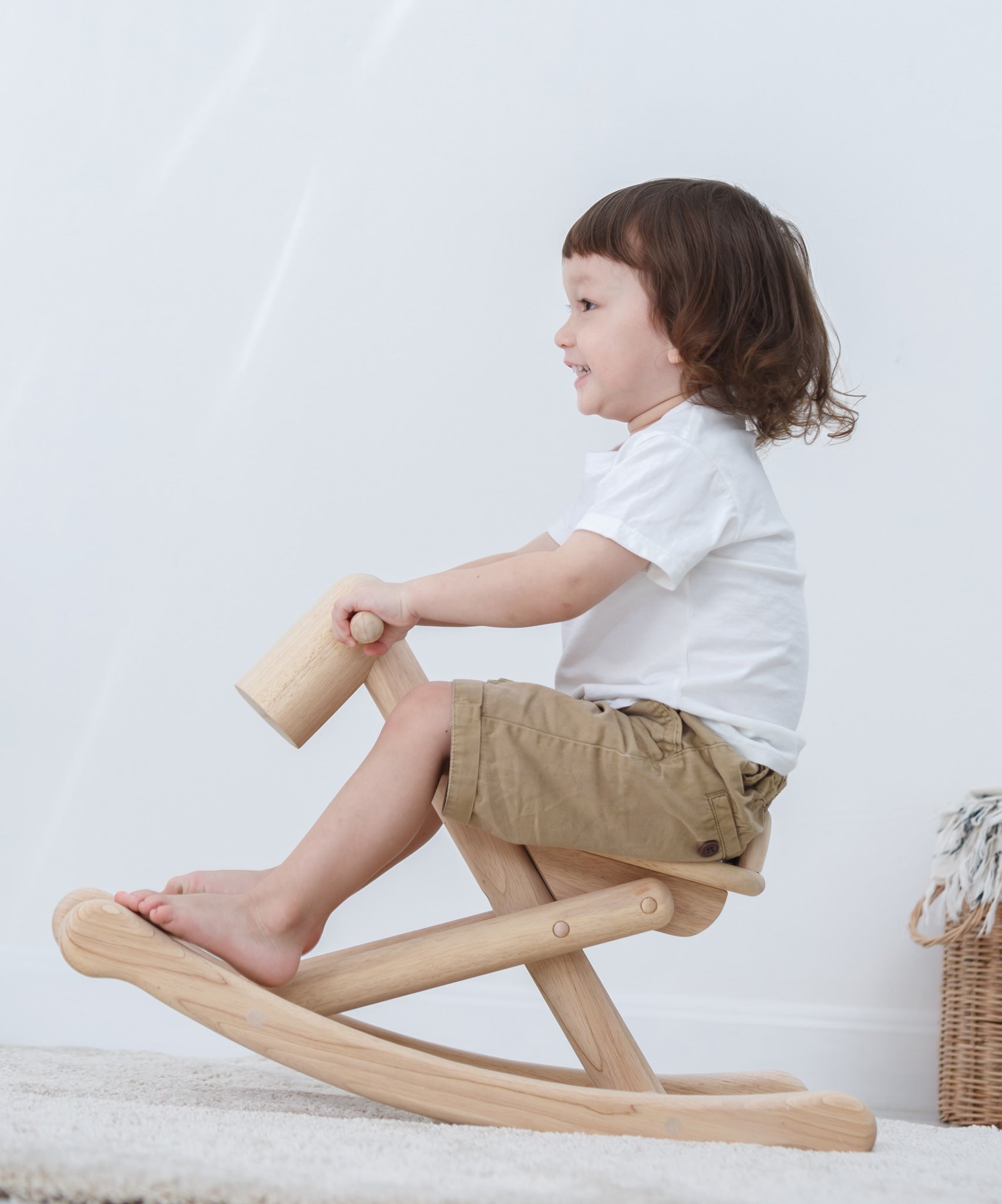 A child is rocking on the PlanToys Foldable Rocking Horse, their feet are placed on the frame at the bottom.