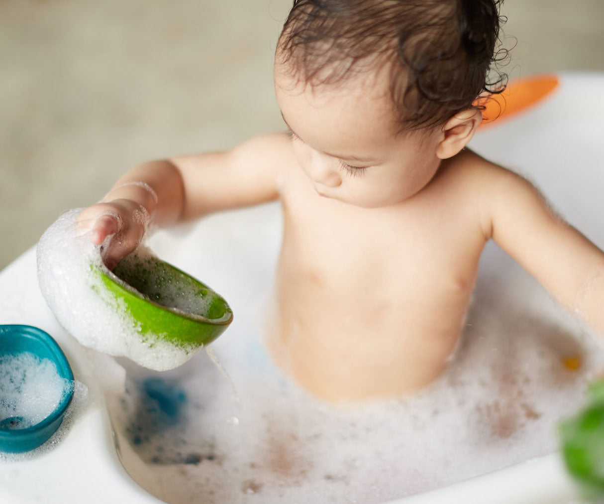 A child in a tub full of bubbly water playing with the PlanToys Fountain Bowl Set. 