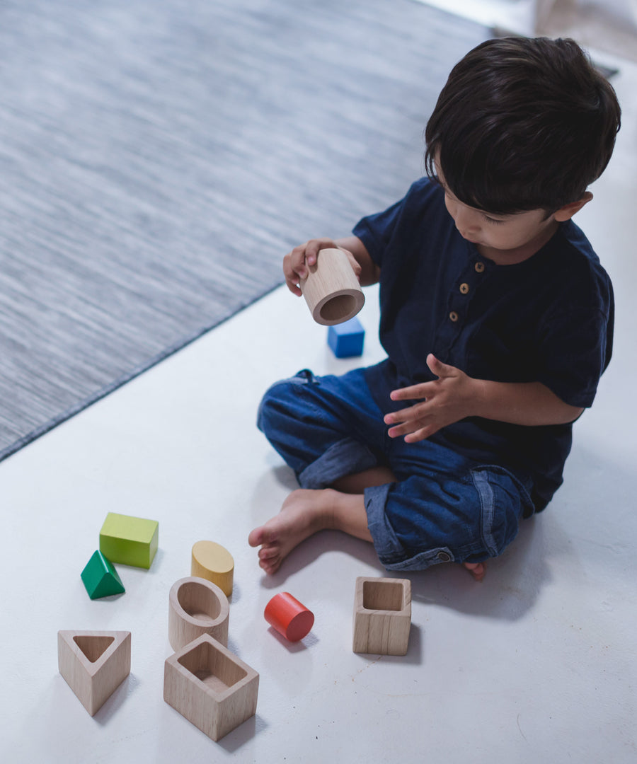 A child sitting on a floor playing with the PlanToys Geo Matching Blocks. 