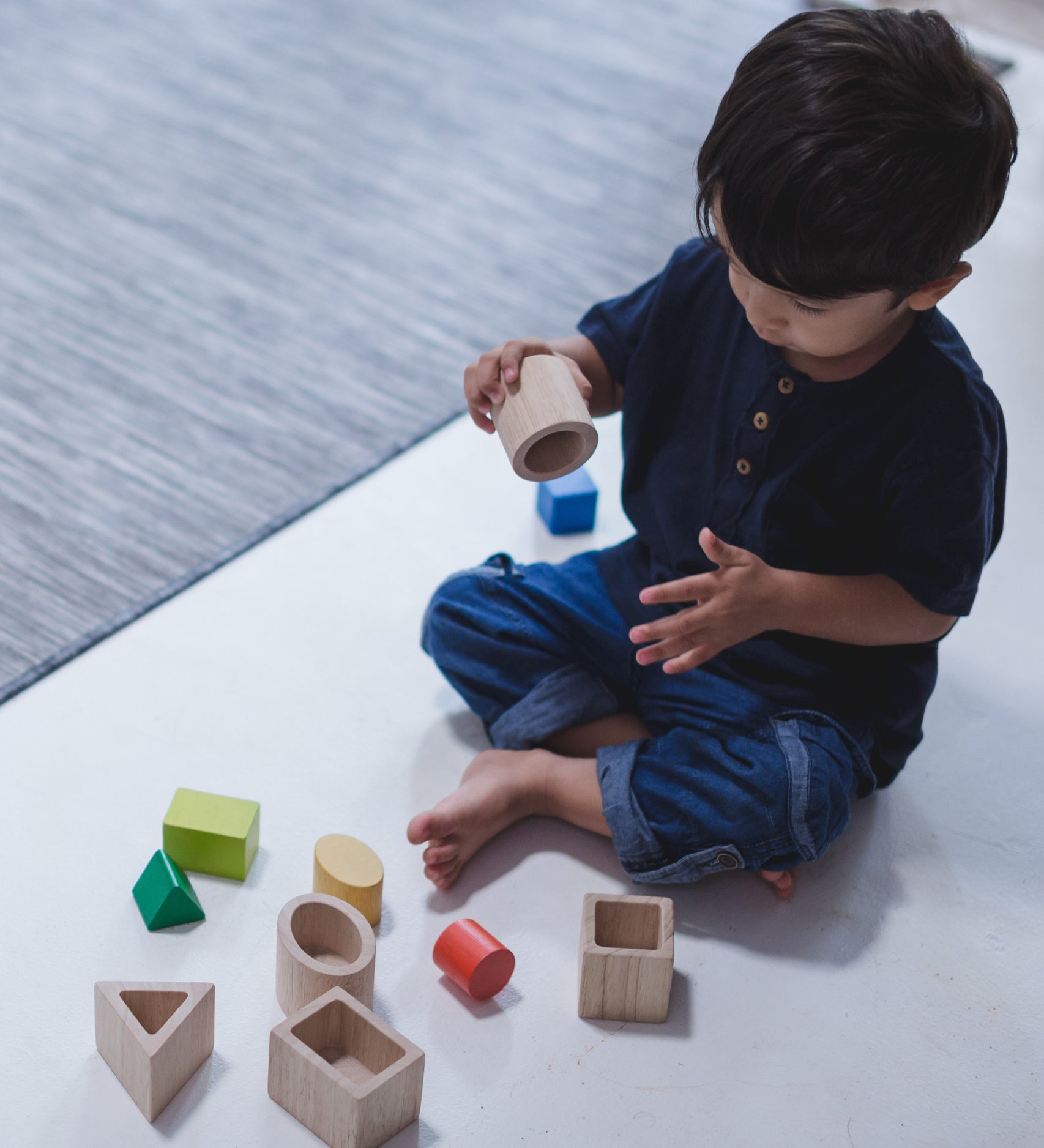 A child sitting on a floor playing with the PlanToys Geo Matching Blocks. 