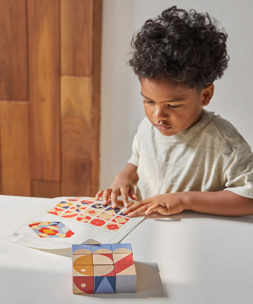 Close up of boy looking at different patterns to make with the PlanToys stacking geo pattern blocks on a white table.