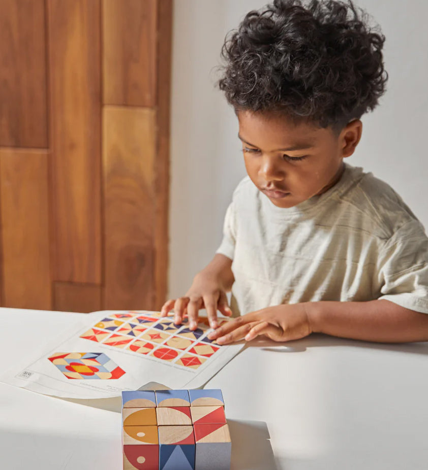 Close up of boy looking at different patterns to make with the PlanToys stacking geo pattern blocks on a white table.