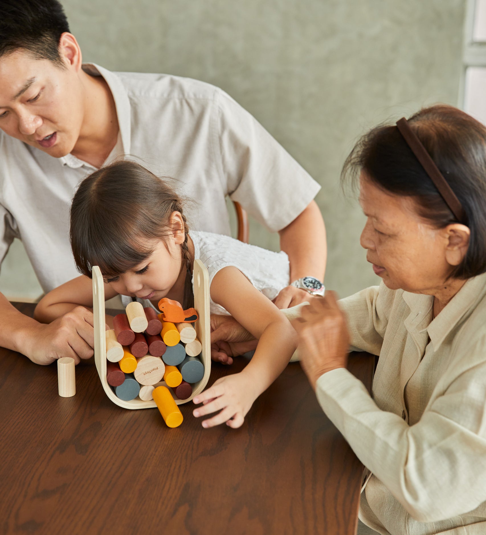 A family sitting around a table playing with the PlanToys Giant Beaver Tumble game. 