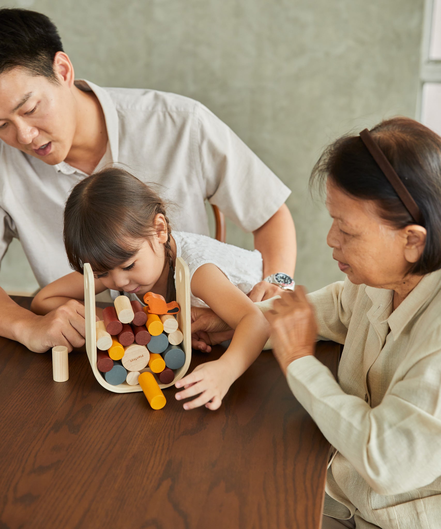 A family sitting around a table playing with the PlanToys Giant Beaver Tumble game. 