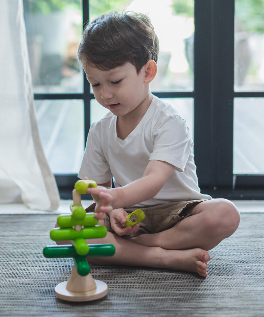 A child playing with the PlanToys Stacking Tree Wooden Toy. The child is placing the green pieces onto the base piece. 