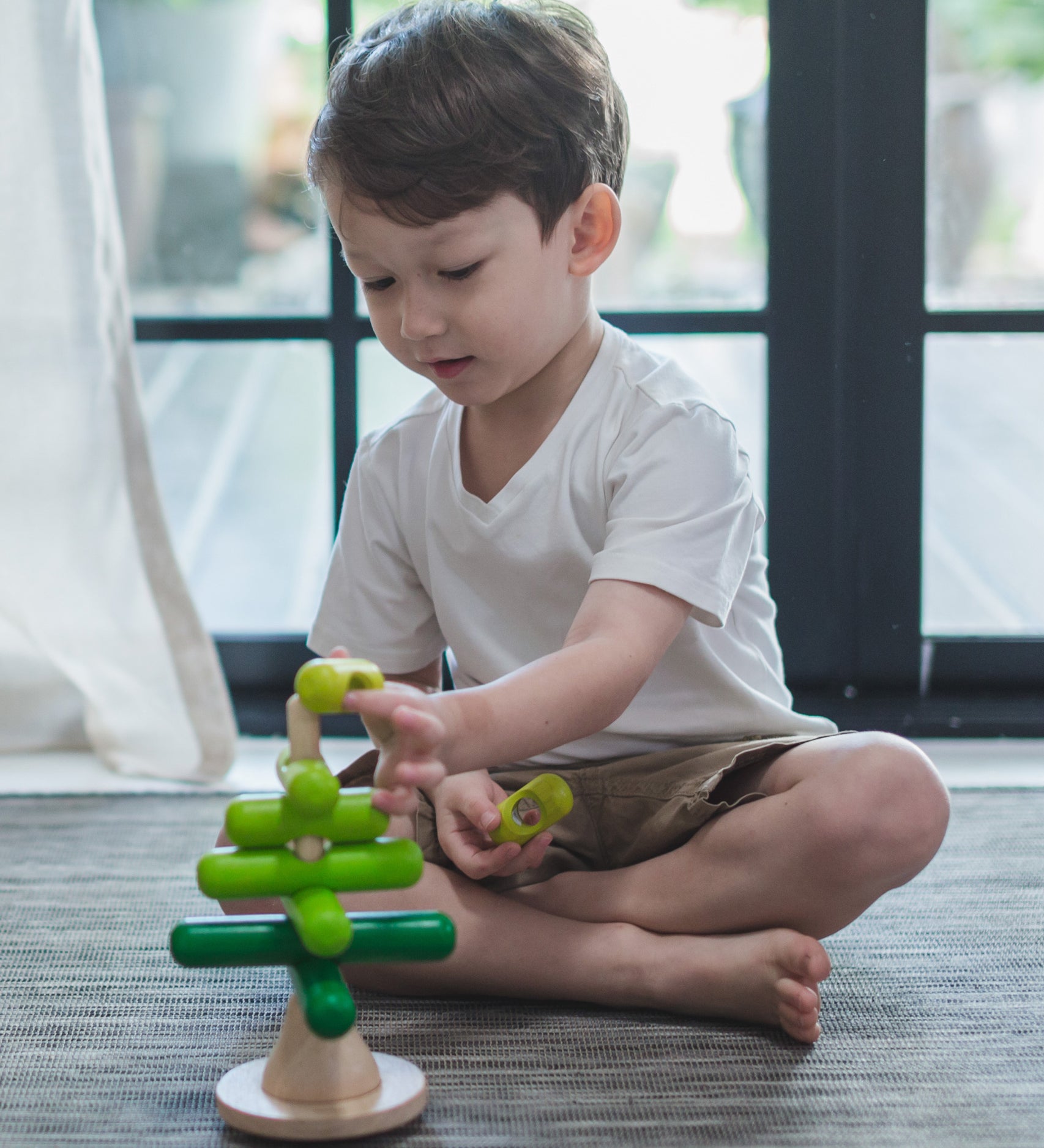 A child playing with the PlanToys Stacking Tree Wooden Toy. The child is placing the green pieces onto the base piece. 