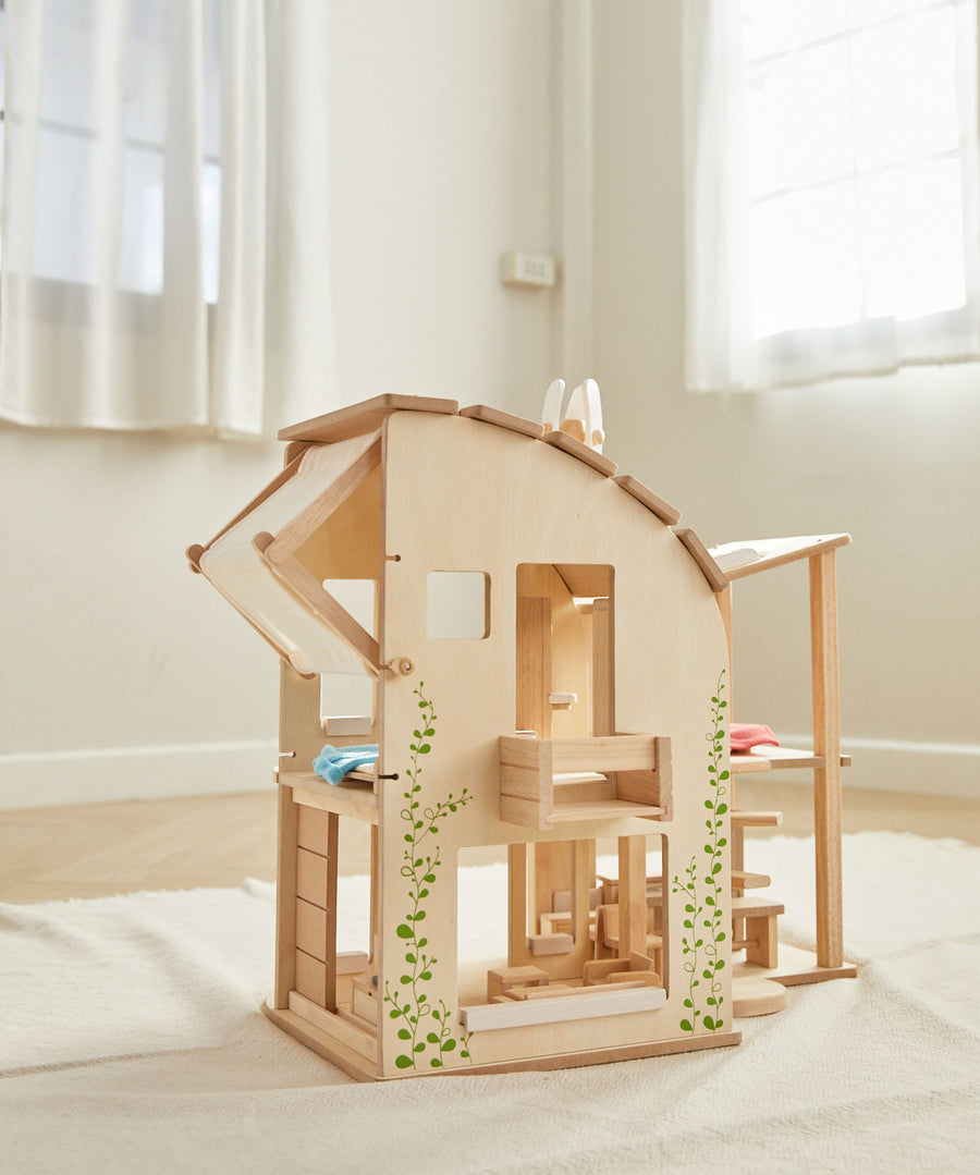 The PlanToys Green Dolls' House and Furniture Set placed on a white rug in the middle of a room.