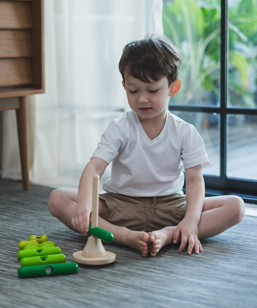 A child playing with the PlanToys Stacking Tree Wooden Toy. The child has placed the longest dark green base on the base. 