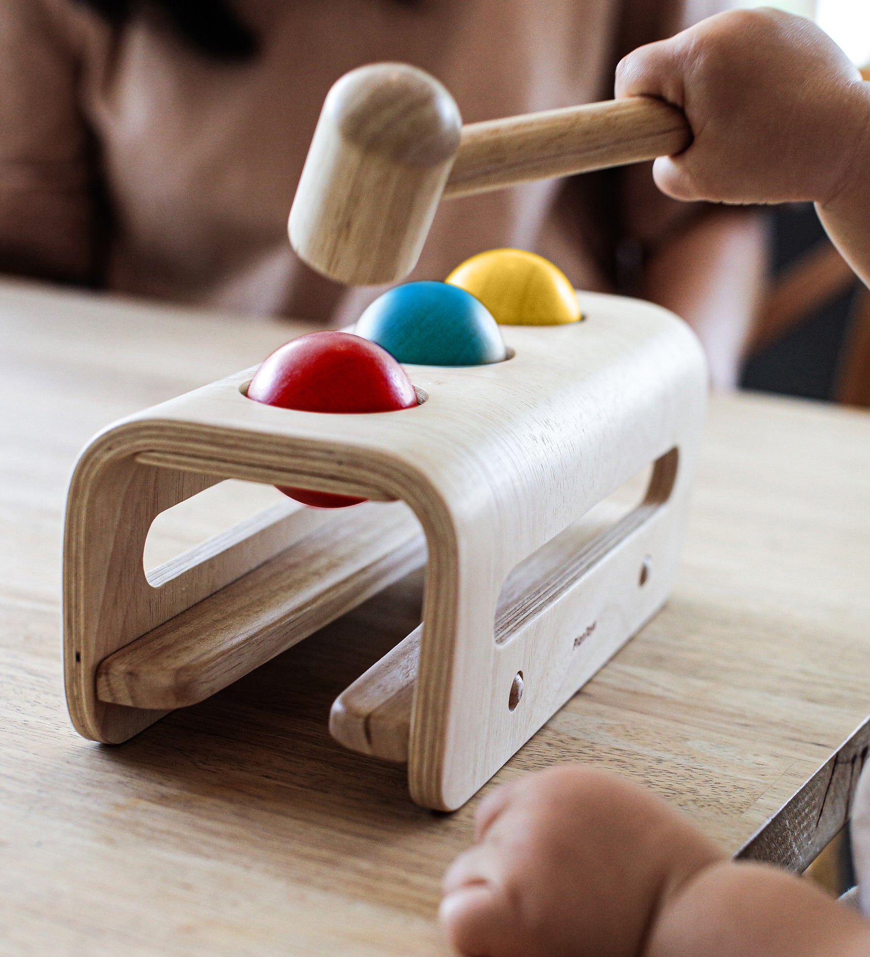 A close up of a child's hands playing with the PlanToys Hammer Balls, they are holding onto the hammer aiming at the red ball.