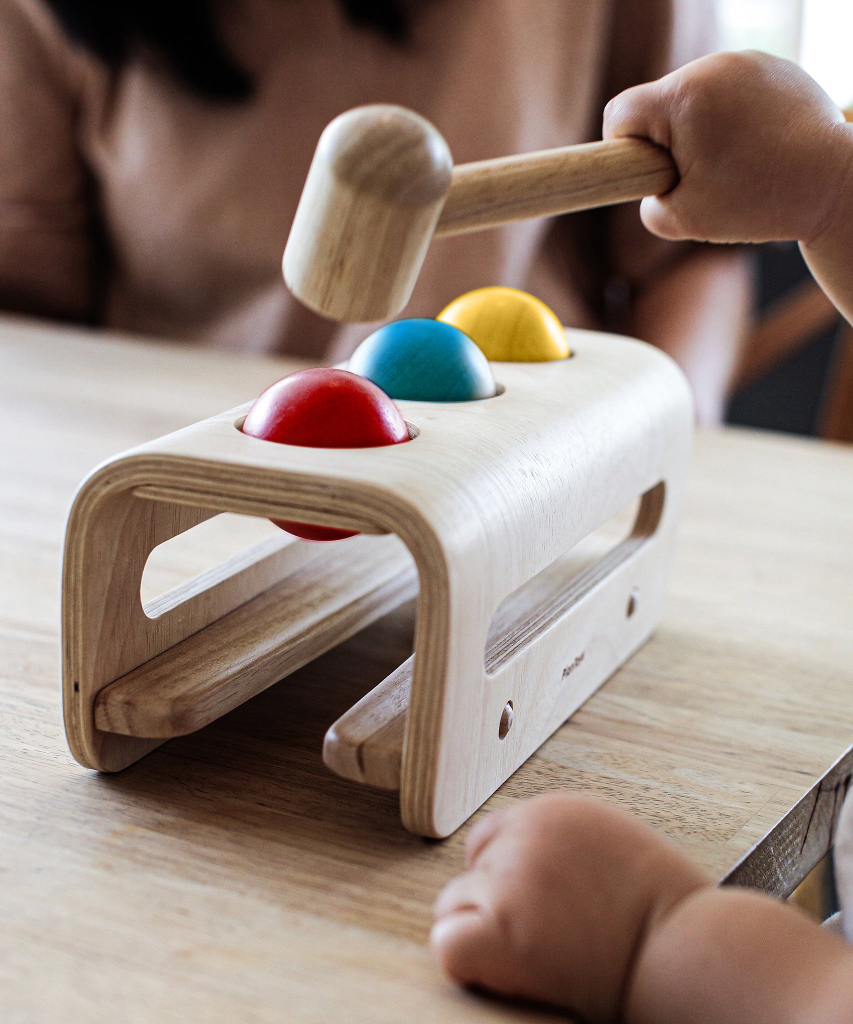 A close up of a child's hands playing with the PlanToys Hammer Balls, they are holding onto the hammer aiming at the red ball.