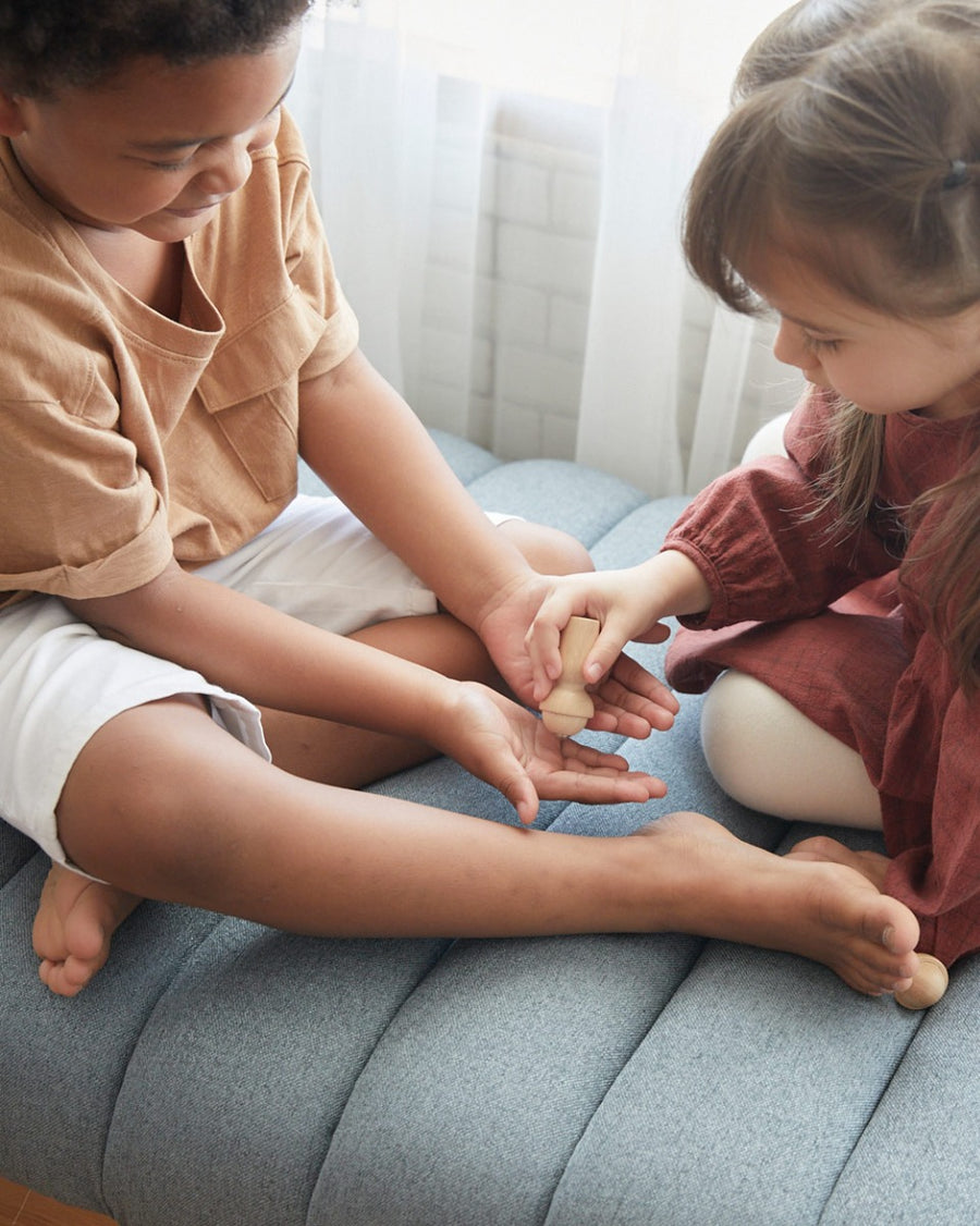 Close up of children playing with the PlanToys wooden touch and guess sensory game on a grey sofa.