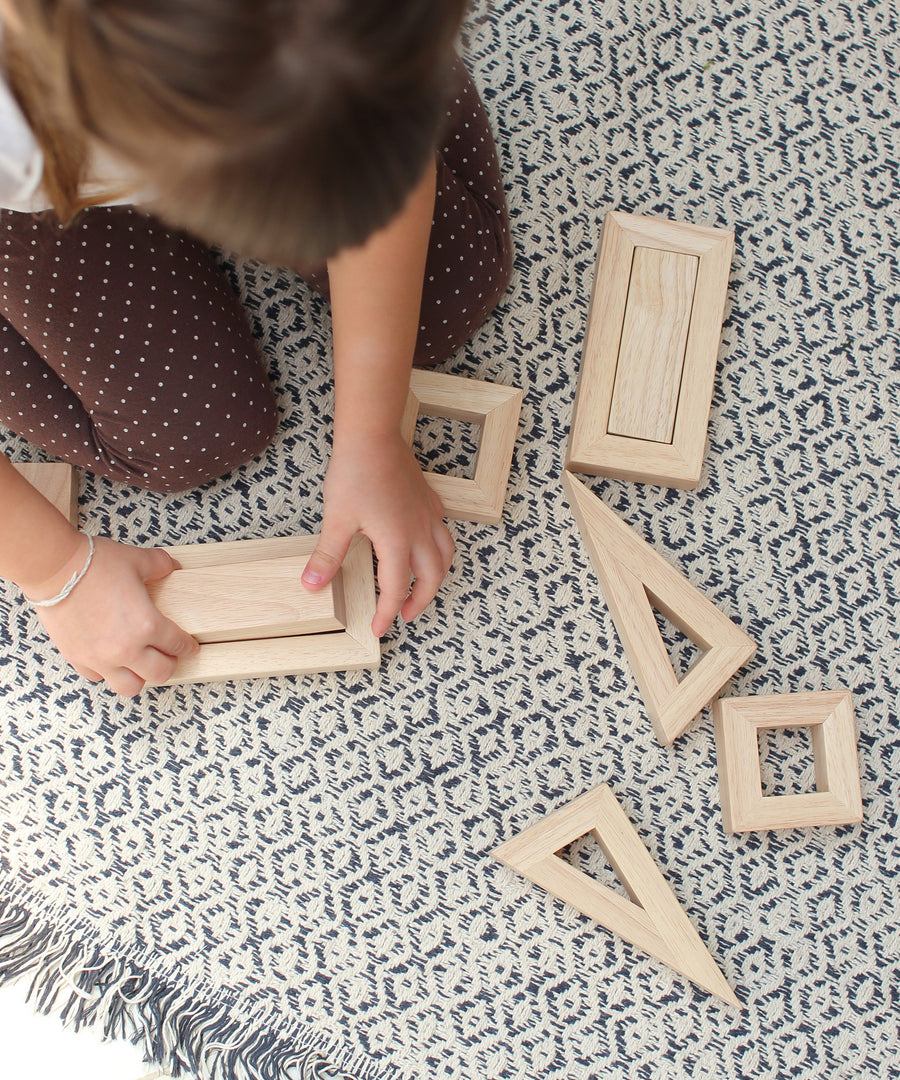 An overhead view of a child sitting on a patterned rug playing with the PlanToys Hollow Blocks.