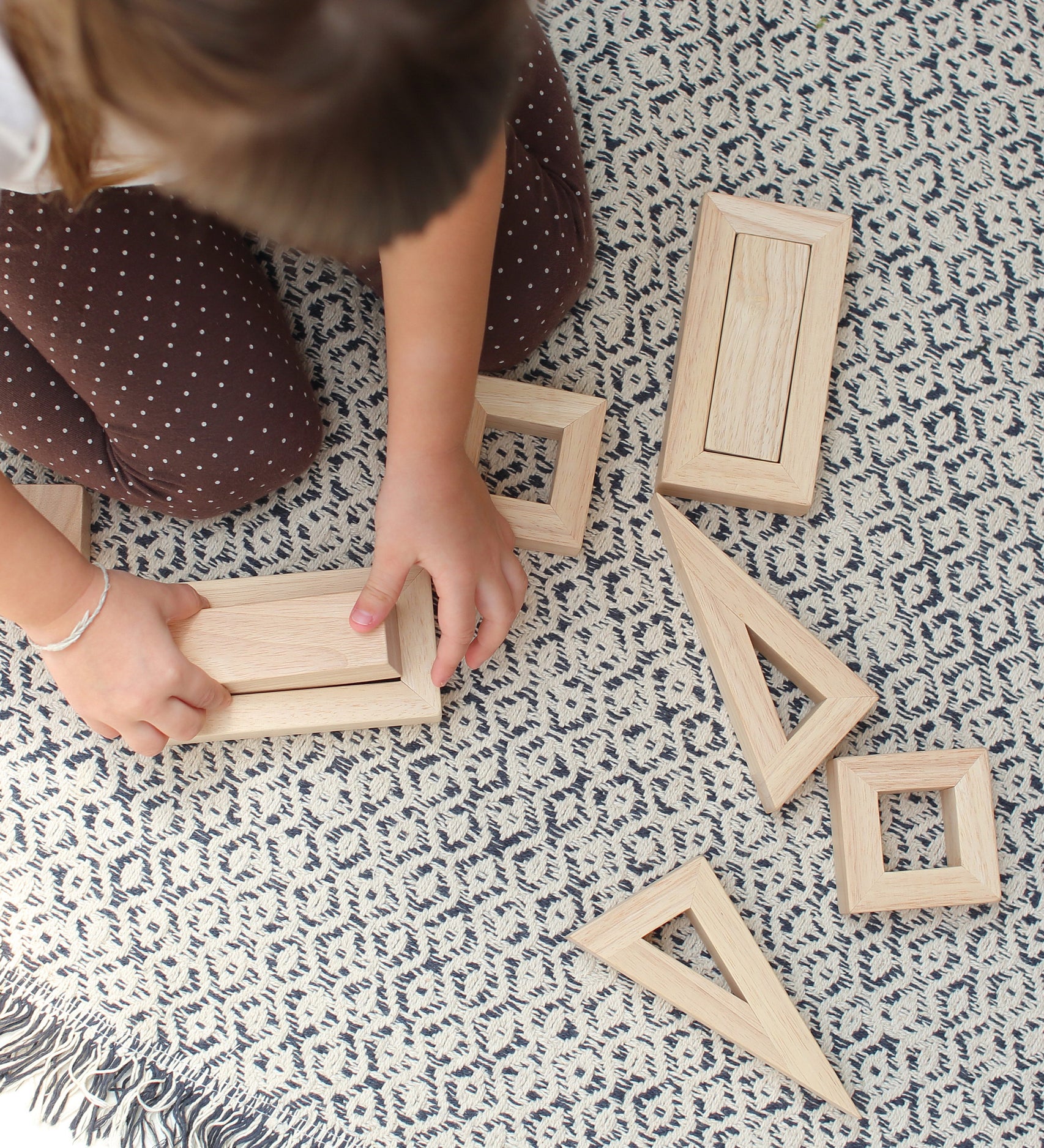 An overhead view of a child sitting on a patterned rug playing with the PlanToys Hollow Blocks.