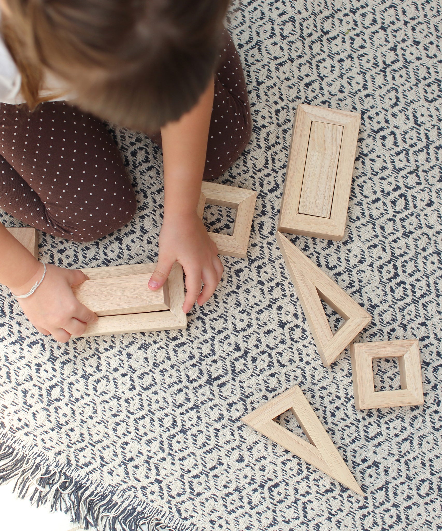 An overhead view of a child sitting on a patterned rug playing with the PlanToys Hollow Blocks.