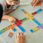 Close up of a family sat around the PlanToys rainbow wooden mood dominos game on a grey tablecloth