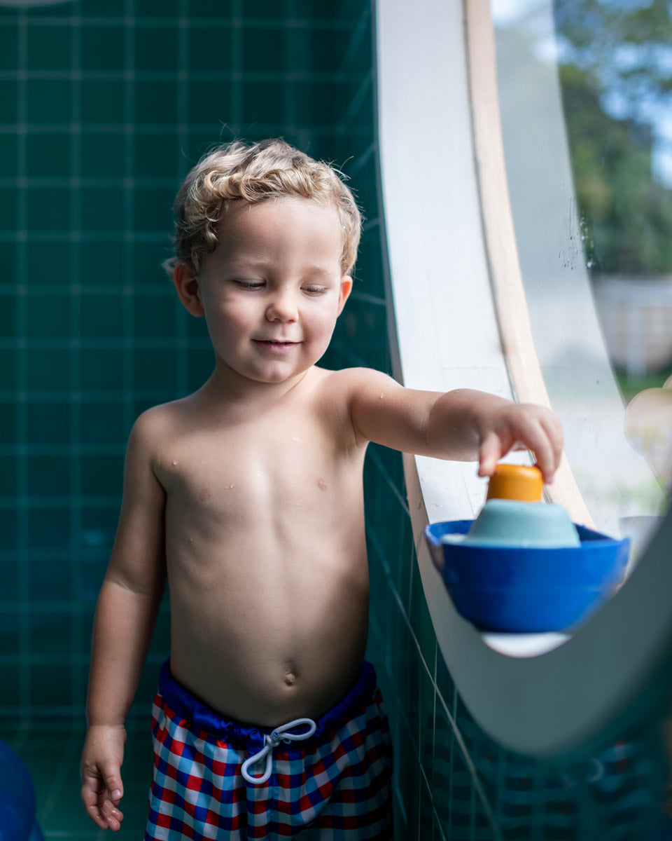 Young boy stood in a round window playing with the PlanToys eco-friendly wooden tugboat