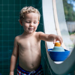 Young boy stood in a round window playing with the PlanToys eco-friendly wooden tugboat