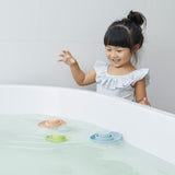 Girl looking at 3 PlanToys eco-friendly rubber boat bath toys floating in some water