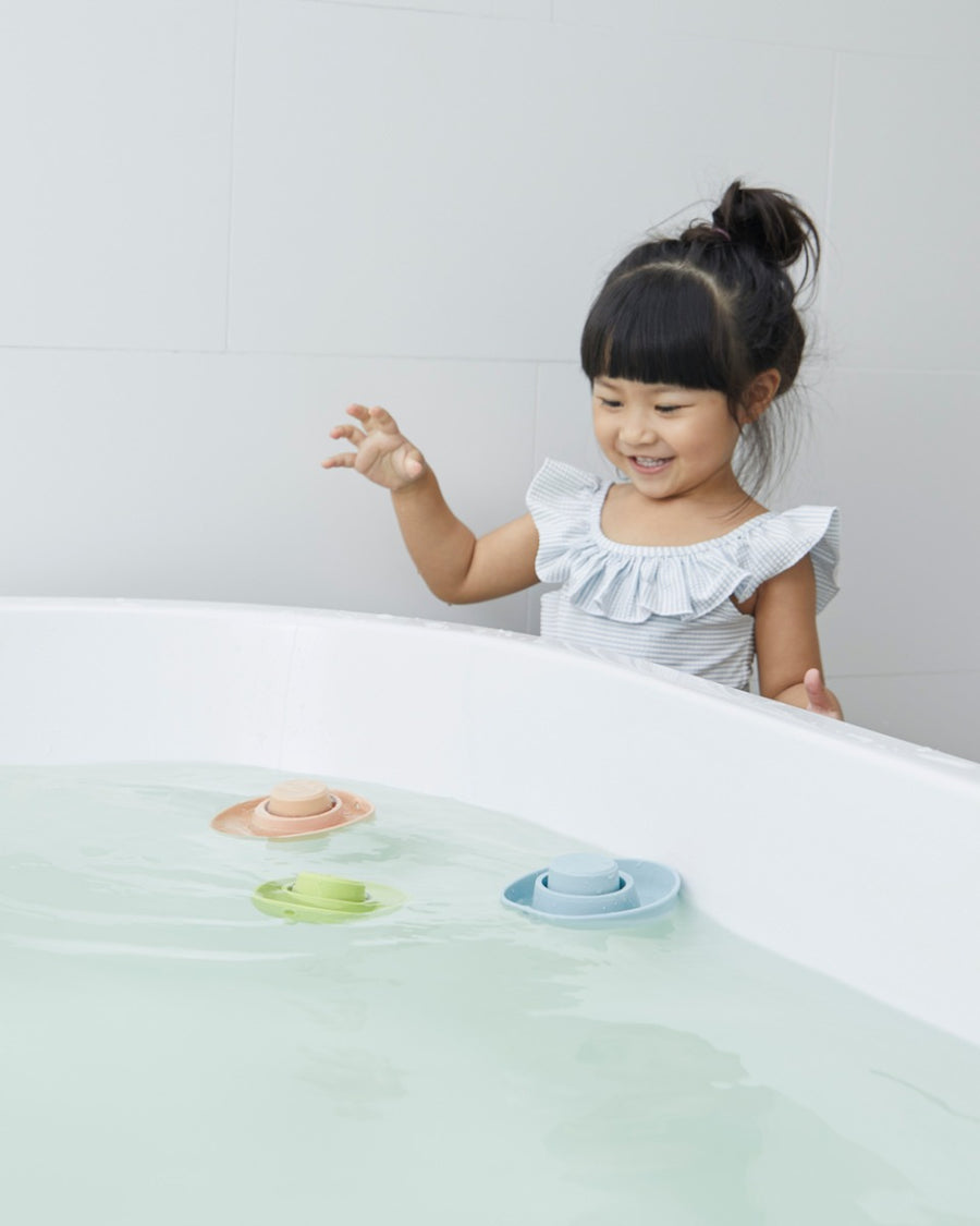 Girl leaning over a bath tub playing with some PlanToys natural rubber boat toys