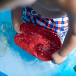 Close up of a young boy playing with the PlanToys plastic-free wooden cargo ship in a blue pool