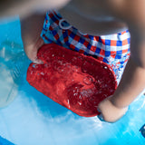 Close up of a young boy playing with the PlanToys plastic-free wooden cargo ship in a blue pool