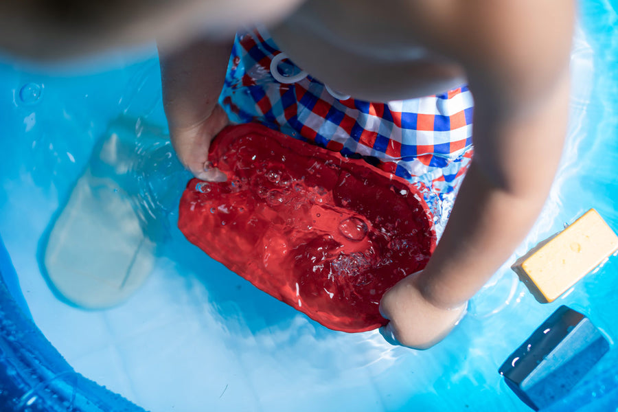 Close up of a young boy playing with the PlanToys plastic-free wooden cargo ship in a blue pool