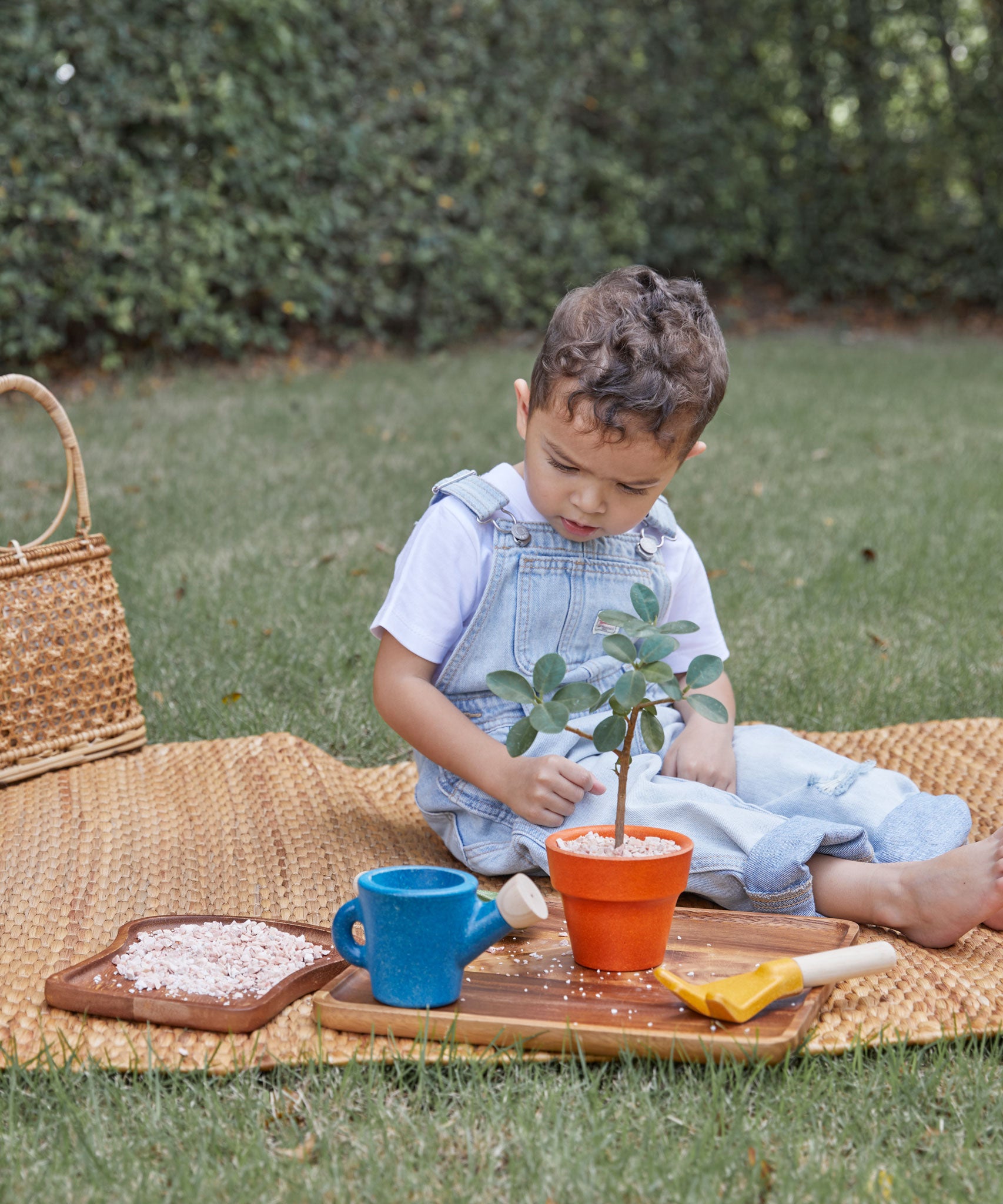 A child playing with the PlanToys Gardening Set, they are sitting on a mat outdoors. 