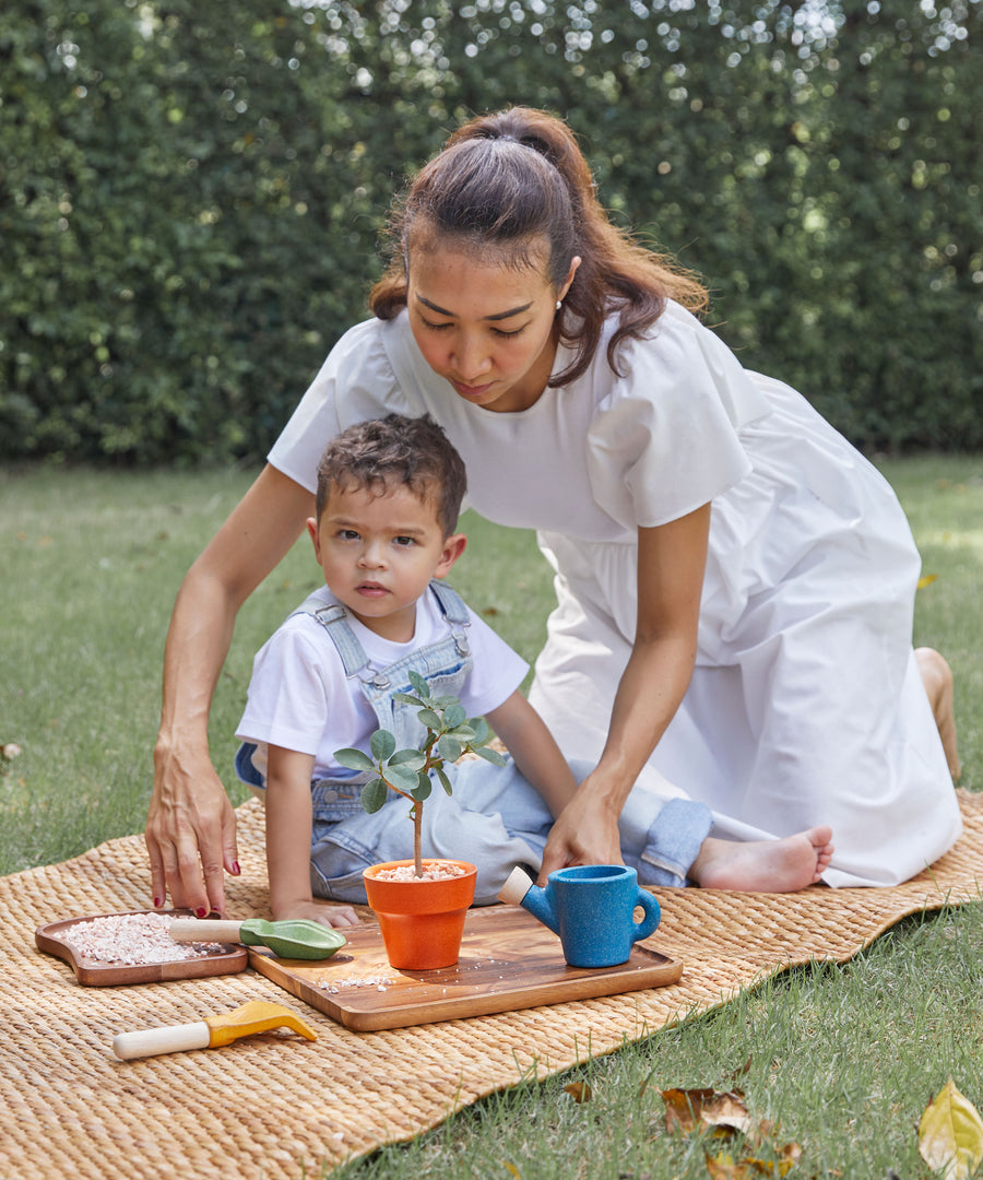 A child playing with the PlanToys Gardening Set, an adult is kneeling over them.