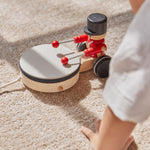 Close up of the PlanToys kids pull along drummer toy on a beige carpet next to a childs hand