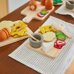 Close up of pieces from the PlanToys wooden charcuterie board toy set laid out on a white table cloth