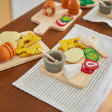 Close up of pieces from the PlanToys wooden charcuterie board toy set laid out on a white table cloth