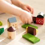 Close up of a childs hands moving pieces of the PlanToys solid wood country side blocks set on a wooden floor