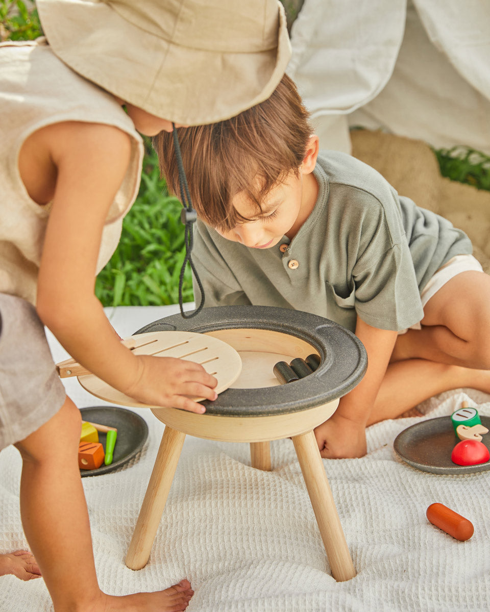 Close up of two children crouched around the PlanToys BBQ toy