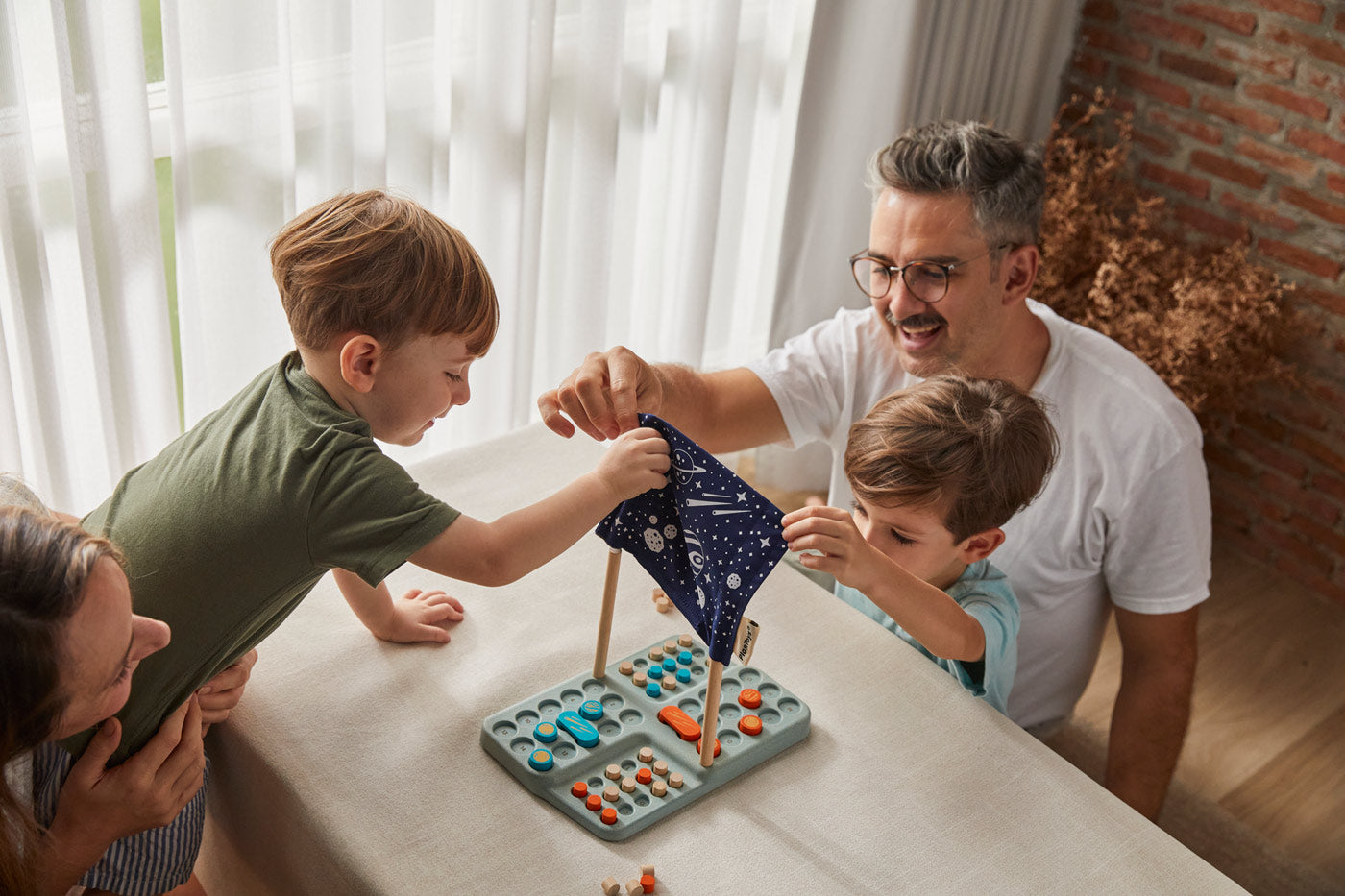 A family sitting around a table playing the PlanToys Guess My Planet Game. 
